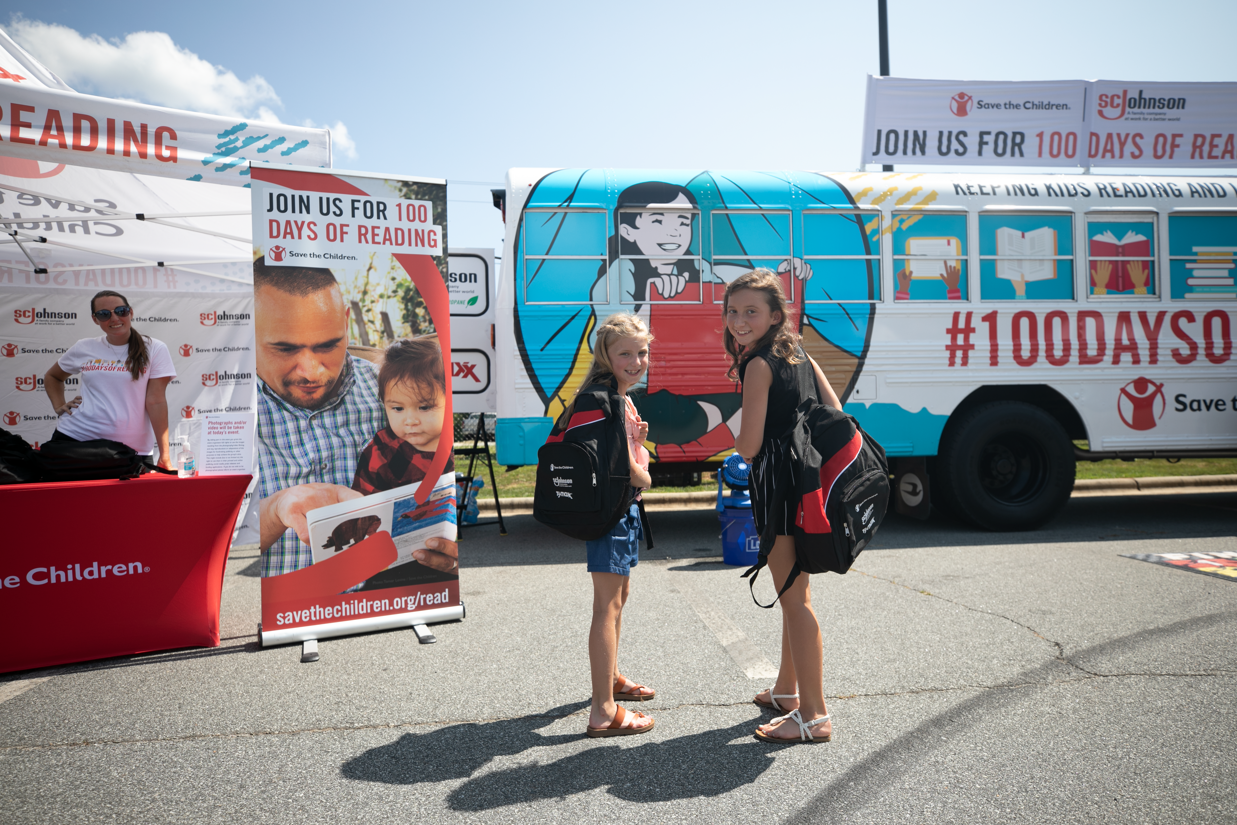 Two girls walking toward bus carrying sc johnson sponsored backpacks